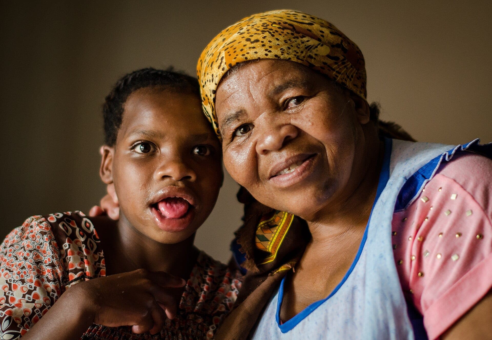 A grandmother and her granddaughter, cheek to cheek, smiling